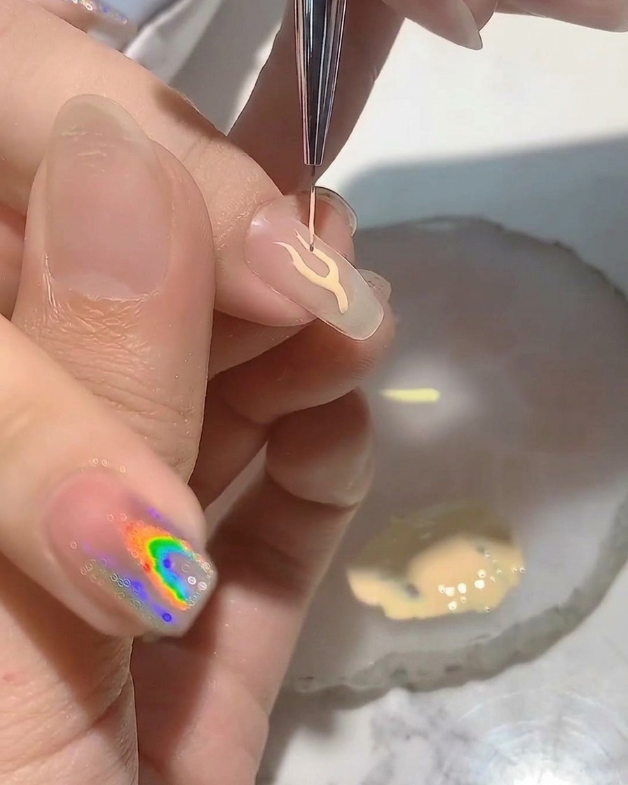 Una nail artist usa un pennello liner fine per dipingere un delicato contorno a forma di fiamma su una tip trasparente.
