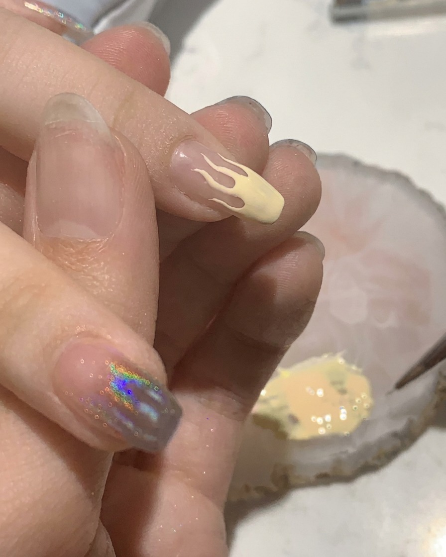 Un piccolo pennello piatto che riempie un design a fiamma color pesca su ununghia appena fatta.