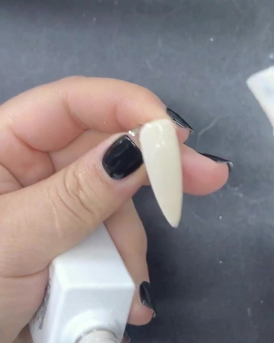 Un primo piano di un pennello che applica uno smalto gel bianco latte velato su ununghia.