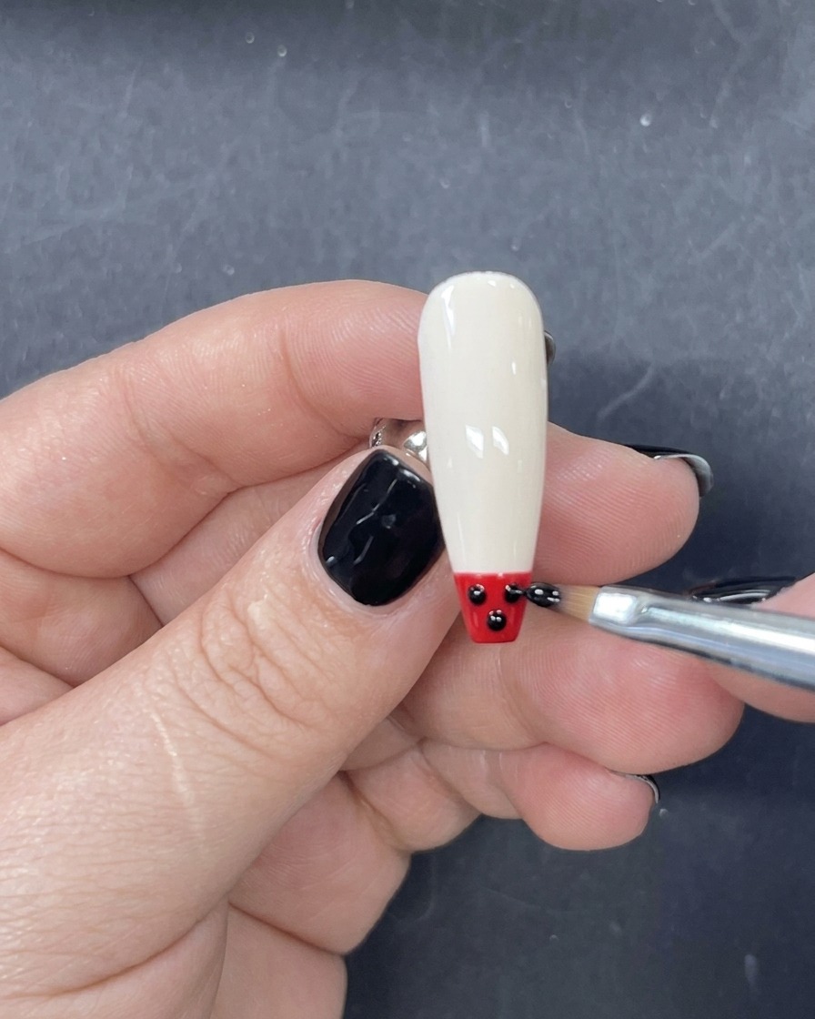 Un pennello liner sottile che applica una striscia orizzontale di smalto gel rosso appena sopra la punta nera sullunghia.