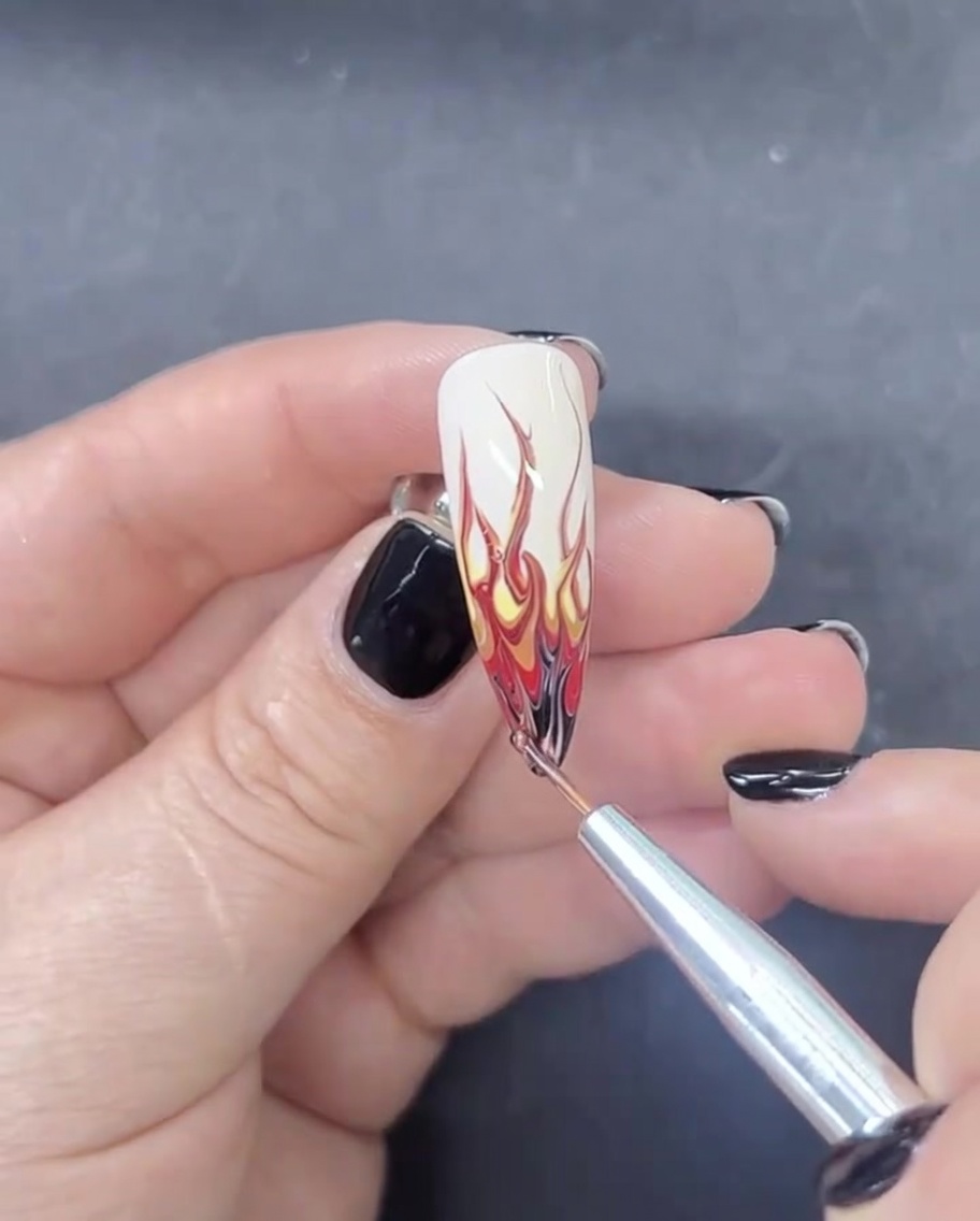 Un pennello liner per unghie che applica una piccola quantità di smalto gel nero sulla punta estrema di ununghia a mandorla per completare un design a fiamma.