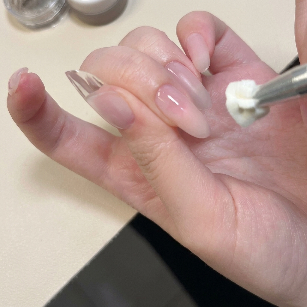 Primo piano di uno strumento in metallo che applica e modella del gel solido bianco sulla punta di ununghia naturale.