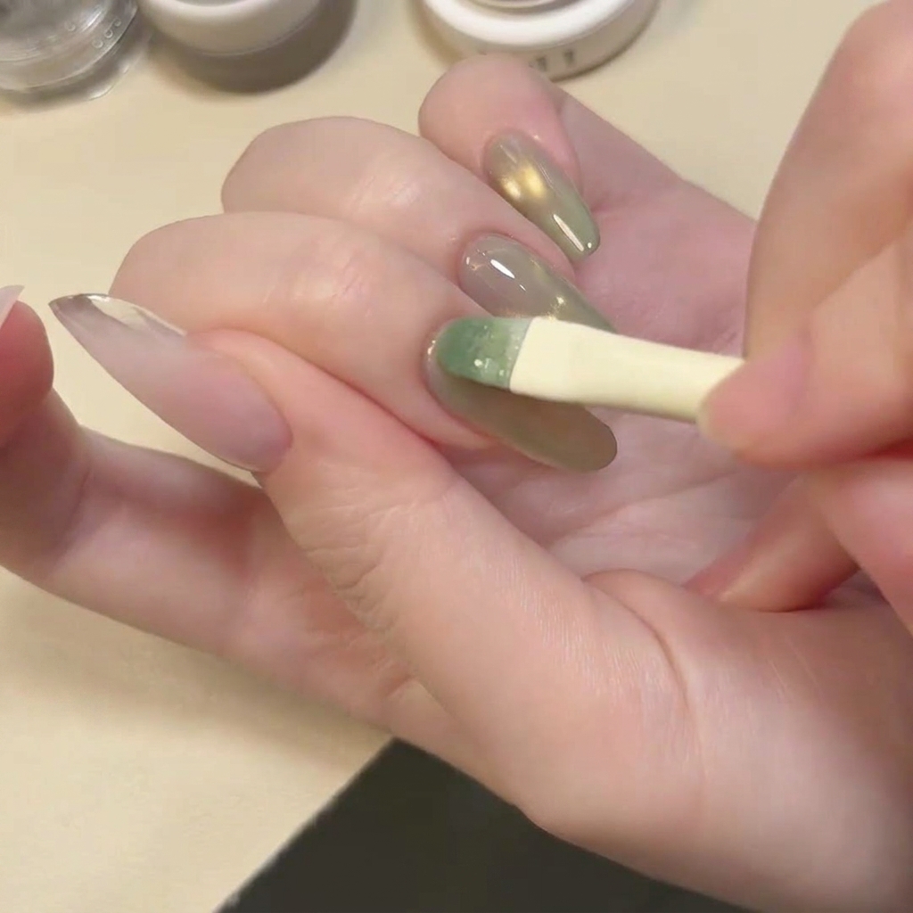 Un pennello che applica uno strato di smalto gel cat eye verde lago traslucido e scintillante sullunghia.