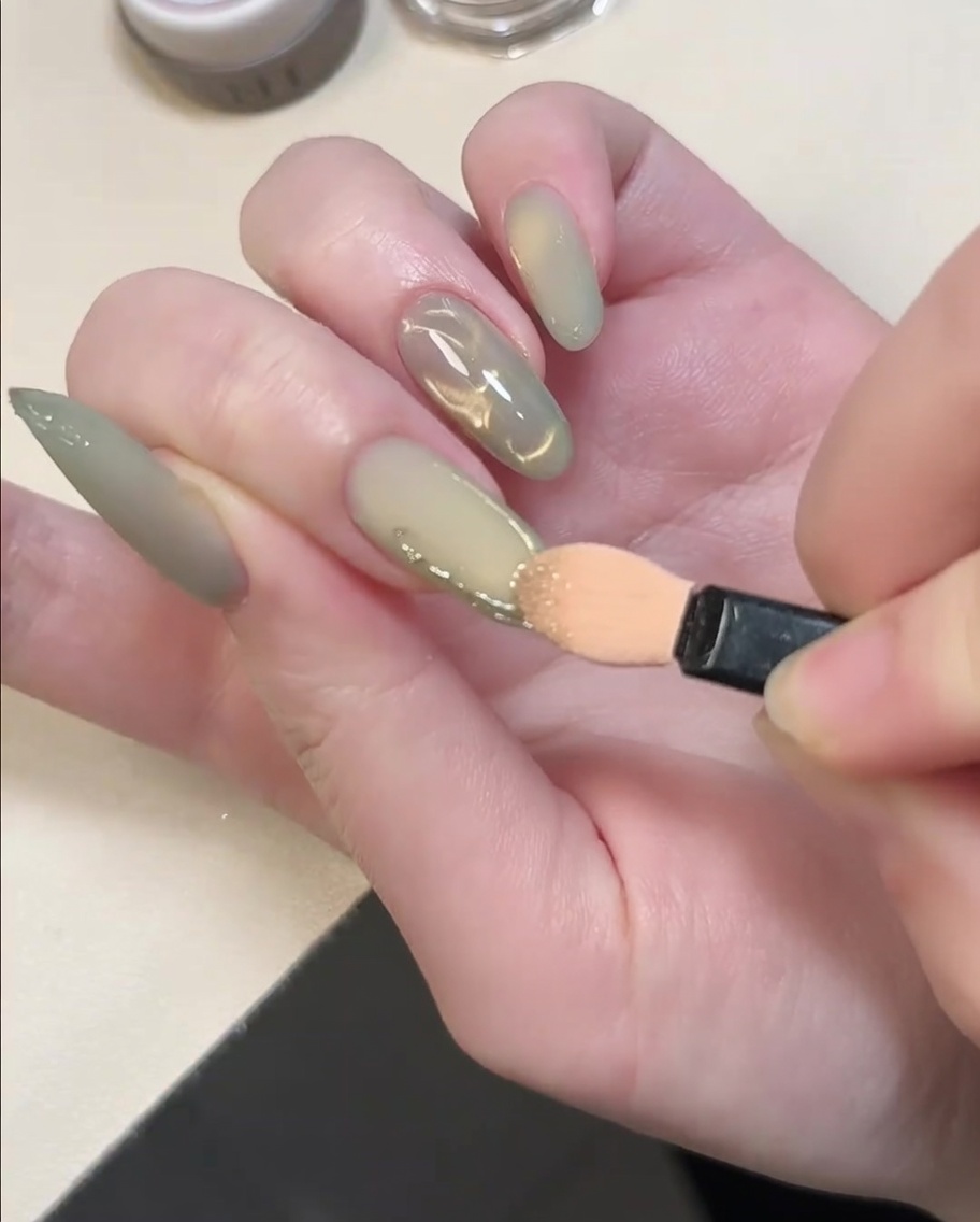Un applicatore per ombretto che sfrega polvere cromo oro sulle linee in gel 3D in rilievo su ununghia.