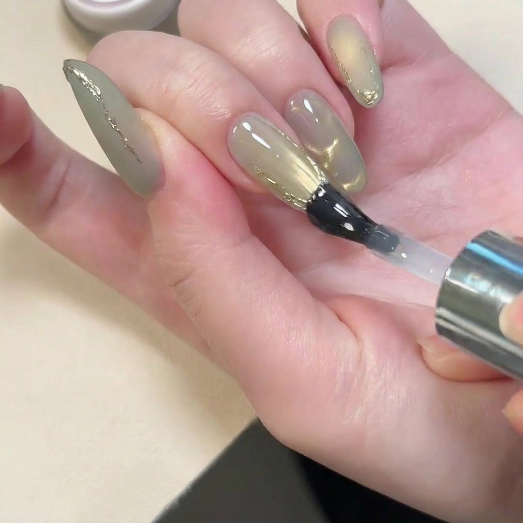 Un pennello che applica un top coat lucido su ununghia con finish opaco e dettagli 3D dorati.
