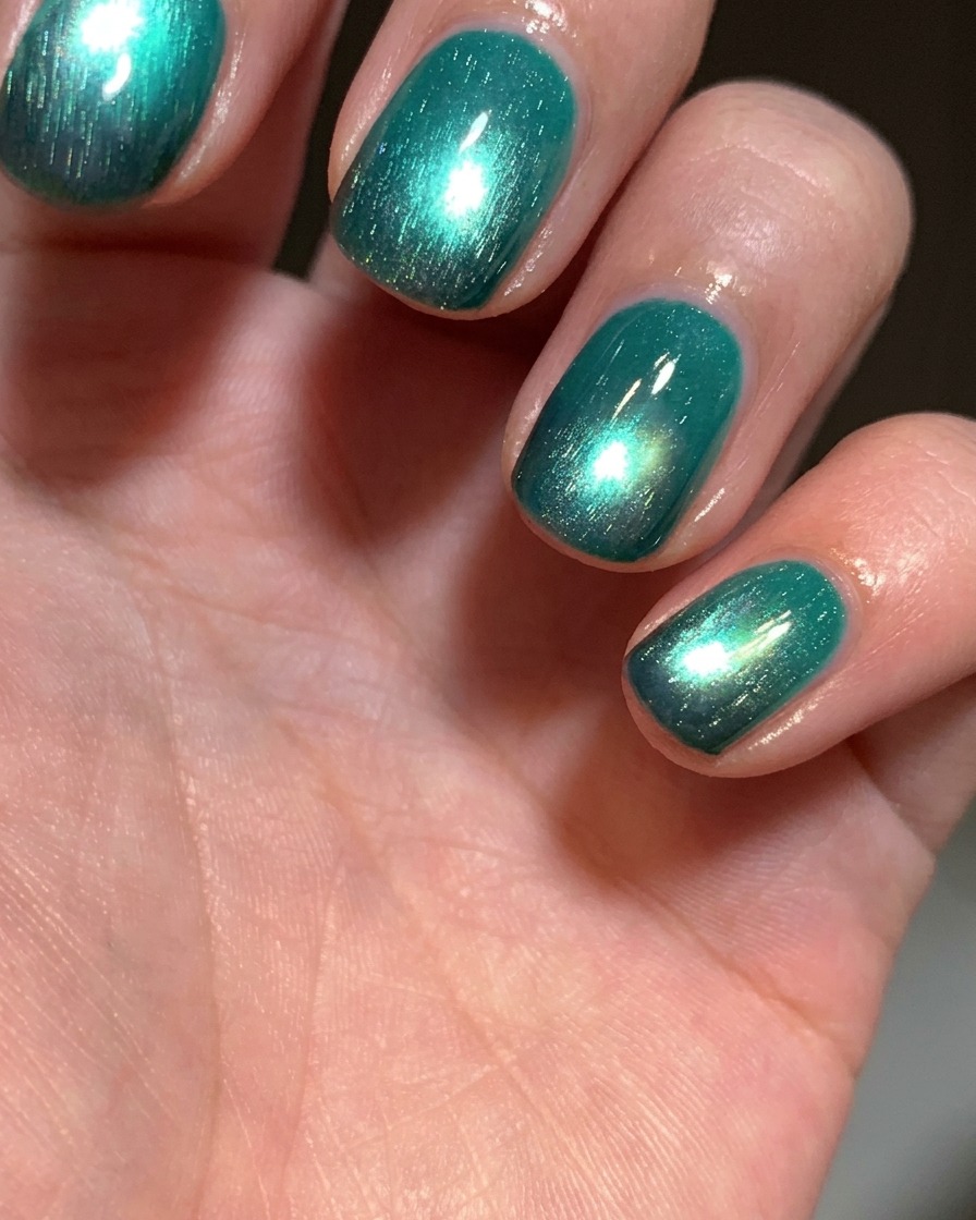 Un pennello che applica uno strato di smalto gel cat-eye verde lago brillante su ununghia che ha una punta nera.