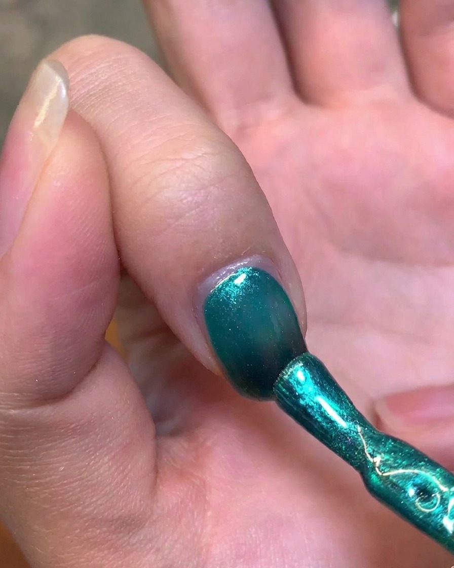Un magnete metallico tenuto vicino al lato di ununghia per manipolare il gel verde in un riflesso cat-eye.