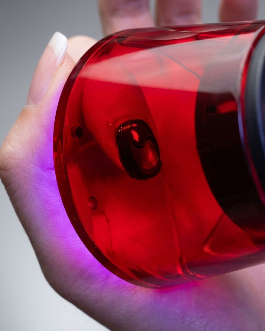 Primo piano di una mano che tiene una lampada UV/LED per unghie compatta e rossa direttamente sopra un dito per polimerizzare lo smalto gel applicato.