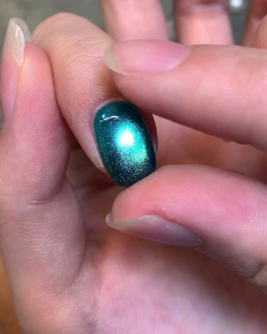 Una vista ravvicinata di un dito che testa delicatamente la consistenza di ununghia gel cat-eye verde scuro finita e lucida.
