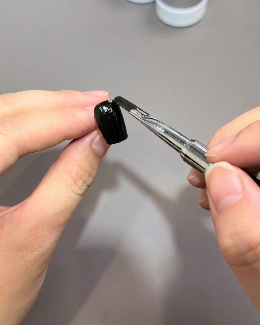 Un pennello da unghie applica uno strato uniforme di smalto gel nero su una superficie ungueale preparata.