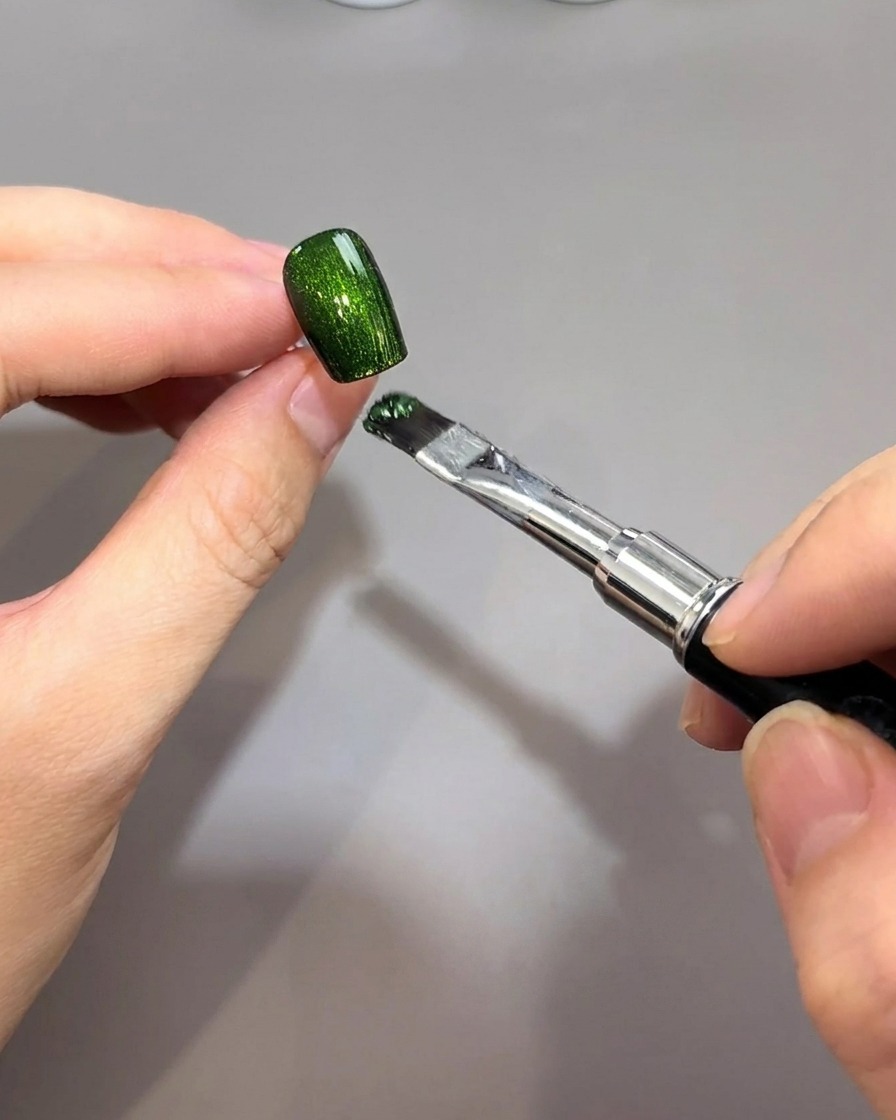 Un pennello applica un gel magnetico verde smeraldo vibrante su una base ungueale nera.