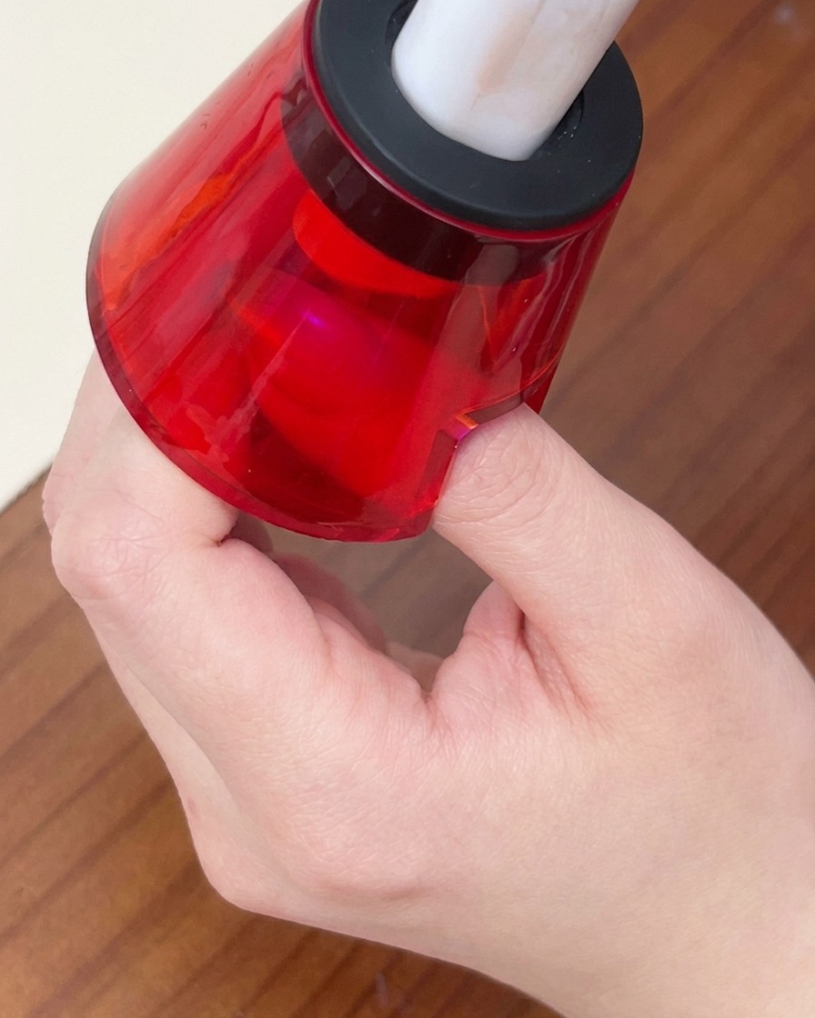 Un dito posizionato sotto una piccola lampada LED portatile rossa per polimerizzare lo smalto gel.