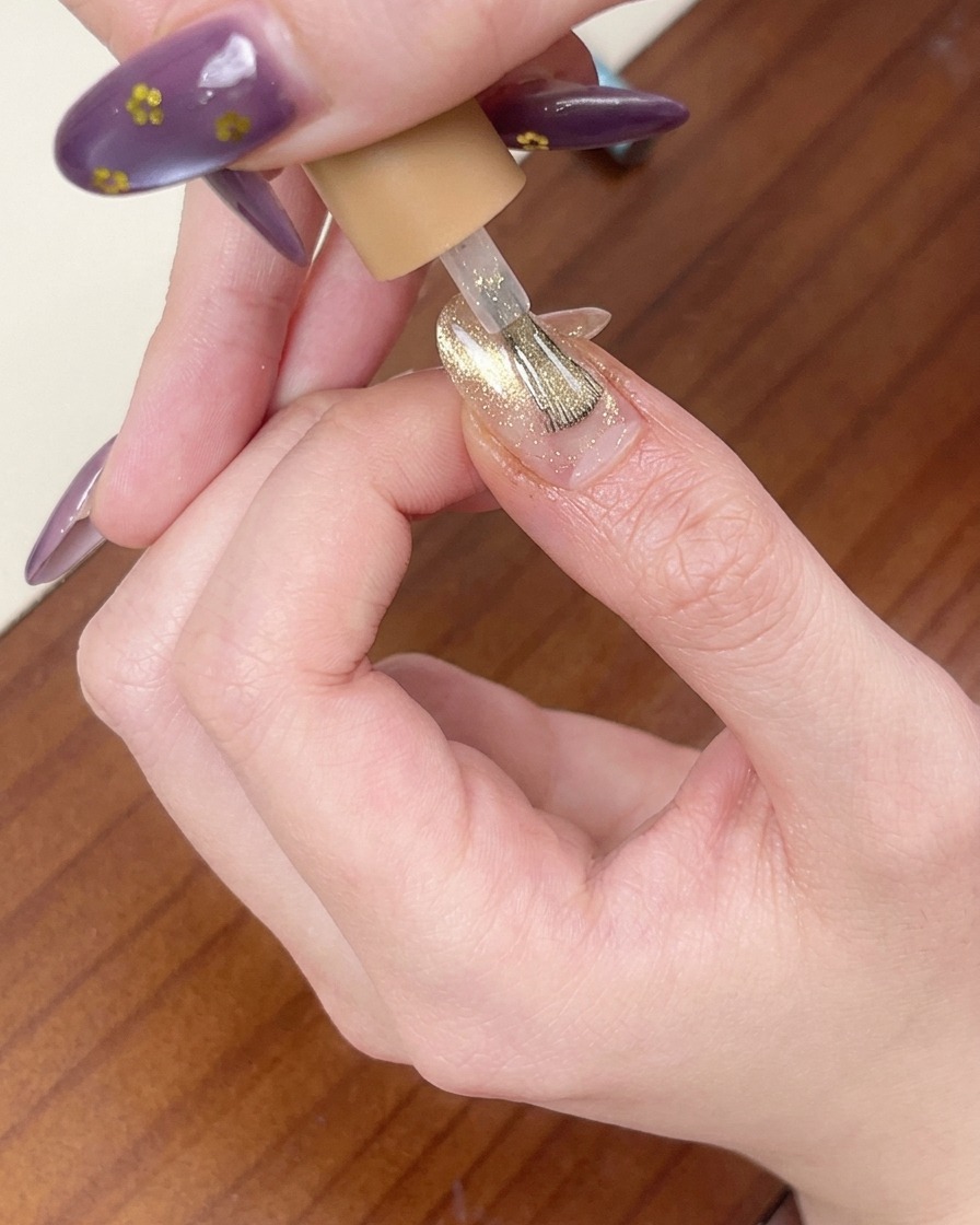 Un pennello applica uno strato di gel cat-eye traslucido rosa oro sopra lunghia.