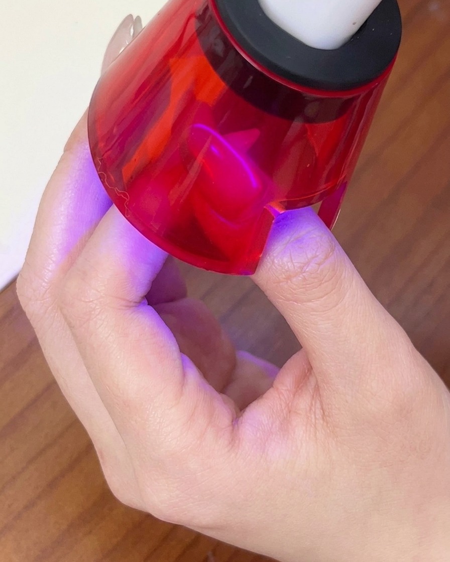 Un dito che polimerizza sotto una lampada LED portatile rossa per fissare il design magnetico.