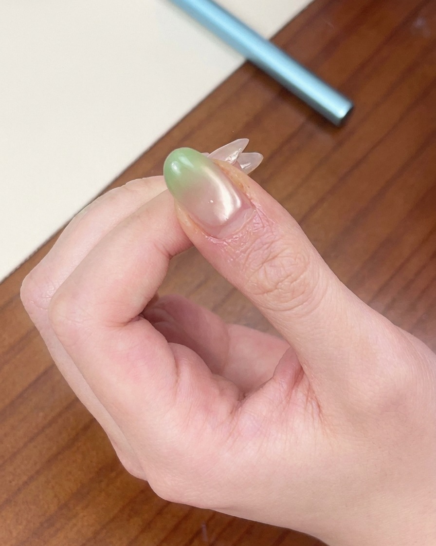 Ununghia con una punta sfumata verde posizionata sotto una mini lampada UV rossa portatile.
