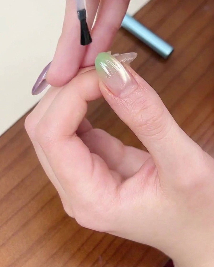 Un pennello che applica uno strato finale di top coat trasparente su ununghia sfumata verde.