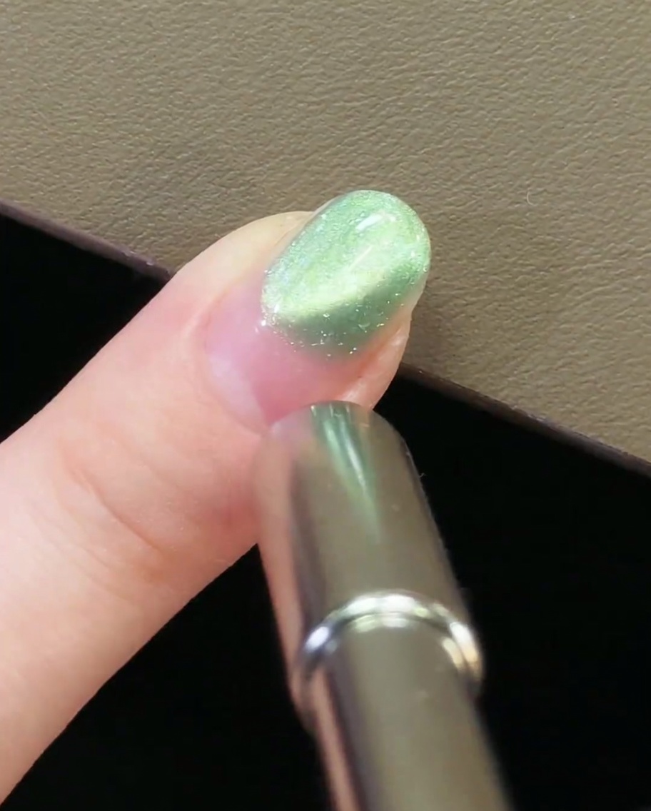 Un magnete per unghie in metallo posizionato nella zona delle cuticole di ununghia con gel cat-eye verde.
