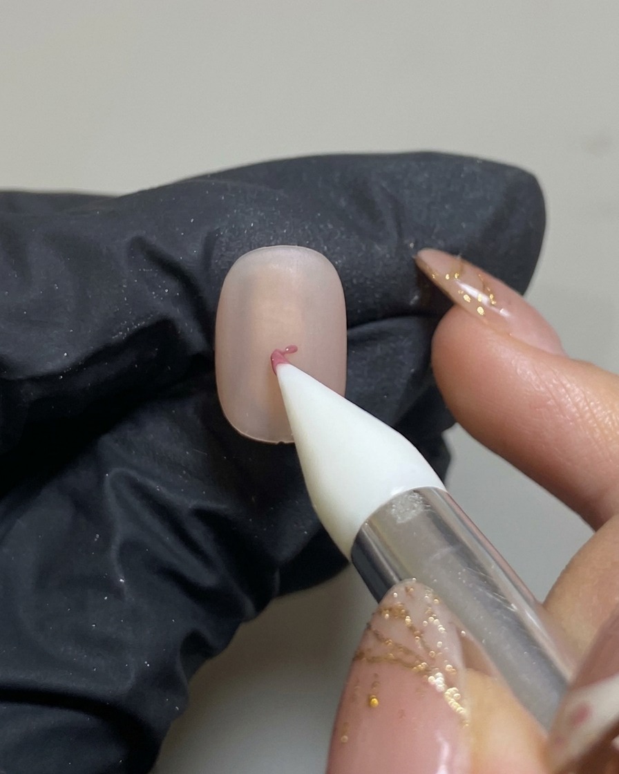 Strumento in silicone che posiziona una piccola goccia di gel rosa al centro dellunghia opaca.