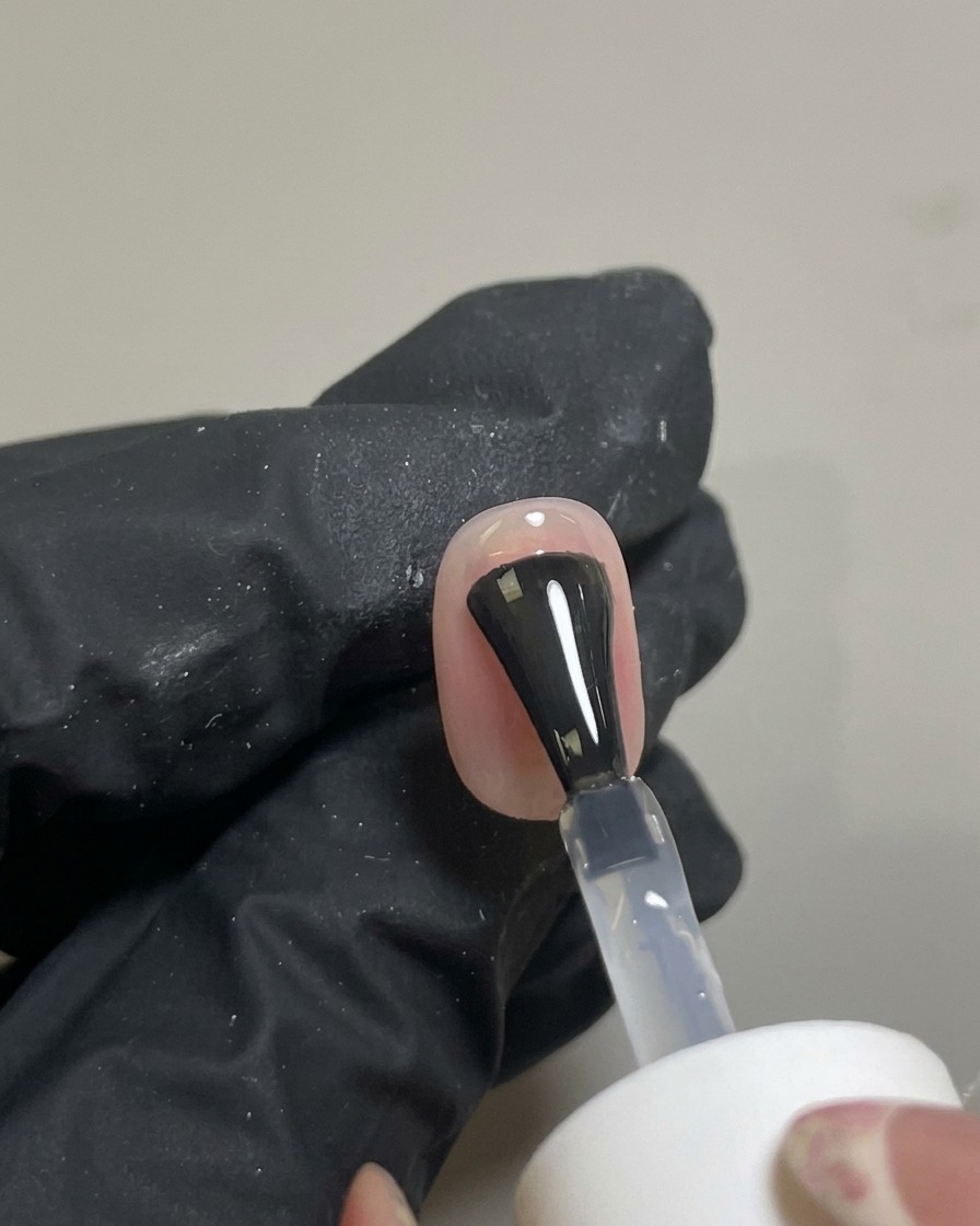 Pennello che applica un top coat trasparente lucido sulla nail art blush finita.