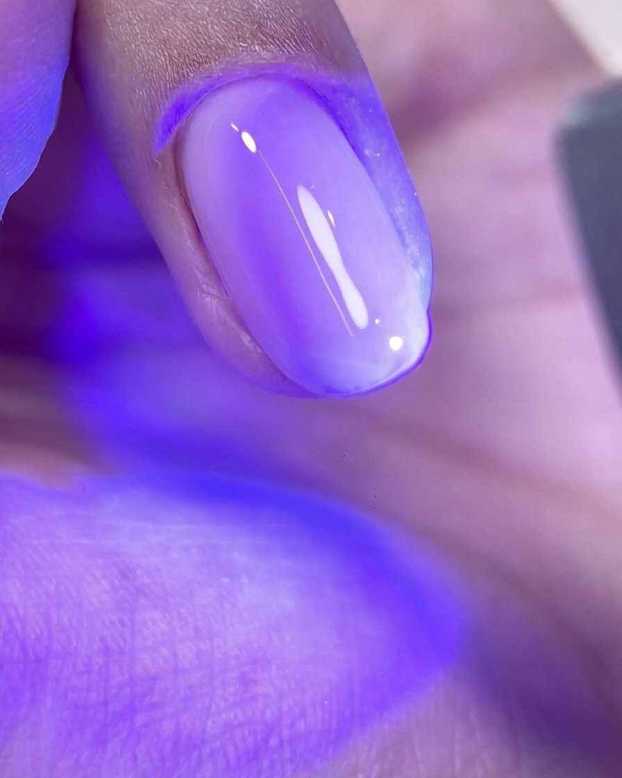 Ununghia con uno strato di gel rosa lucido non polimerizzato sotto la luce viola di una lampada UV/LED.