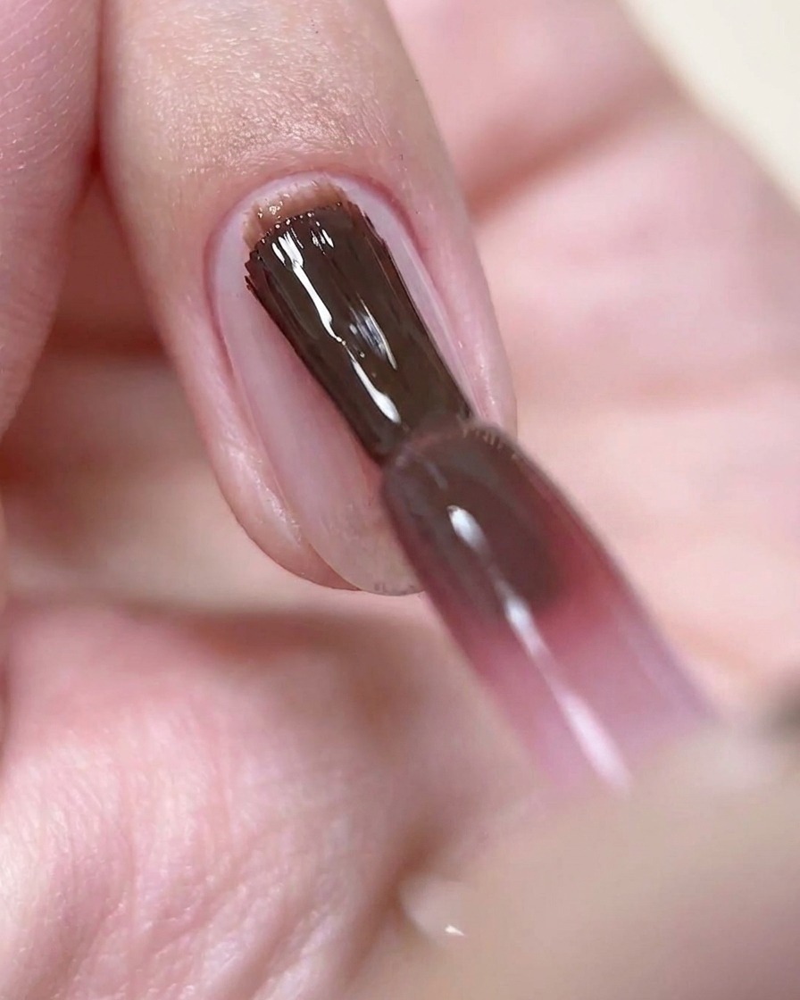 Un pennello da unghie che applica uno strato sottile di gel color rosa vino profondo su ununghia preparata.