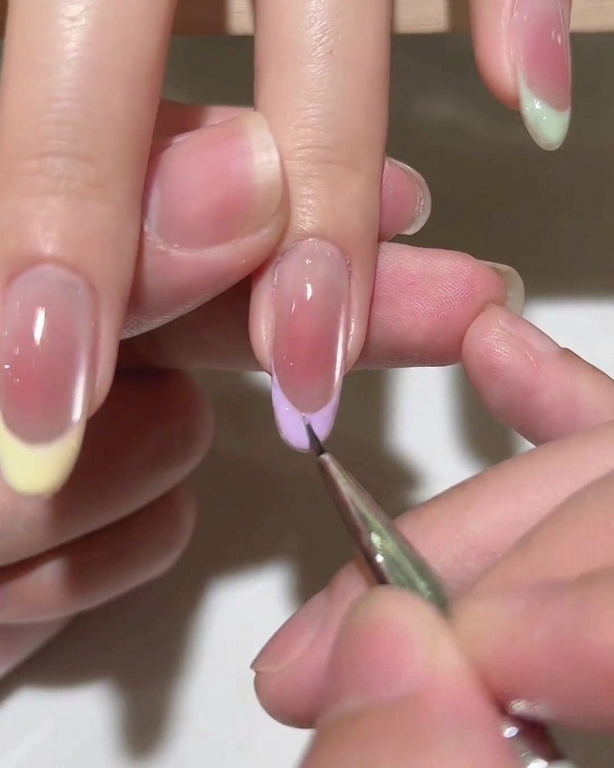 Un pennello applica uno strato di top coat trasparente su una manicure French finita.