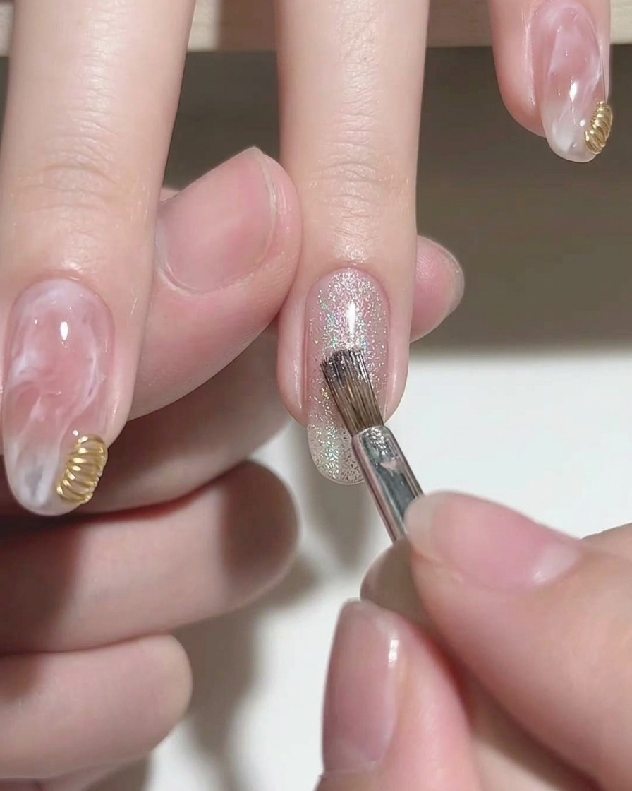 Un pennello che applica un gel cat-eye argentato e brillante sulla punta di ununghia rosa.