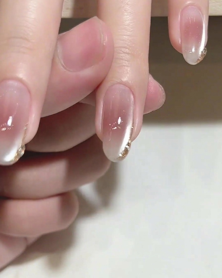 Un pennello che applica un top coat trasparente e lucido su ununghia con delicati dettagli dorati sulle punte.