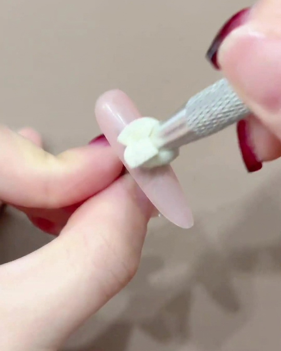Uno strumento con punta in silicone che tampona il pigmento rosa al centro di ununghia.
