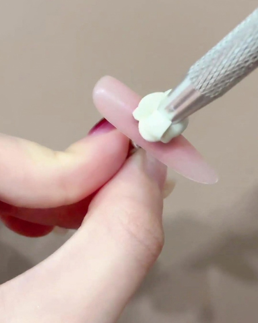 Un pennello che applica un piccolo e preciso punto di gel blush rosa al centro di ununghia.
