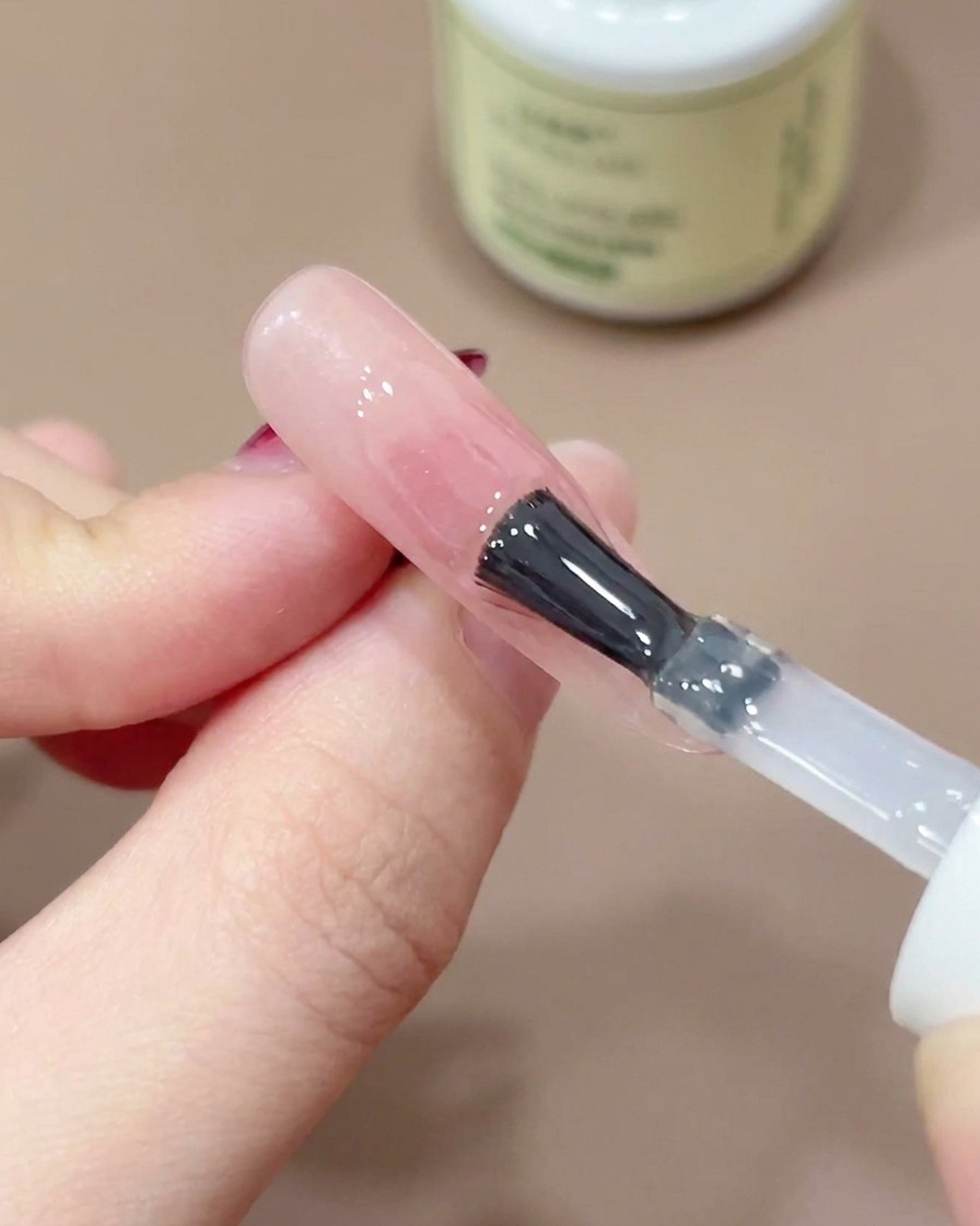 Un pennello per unghie che applica un top coat trasparente e lucido sopra un design blush rosa.