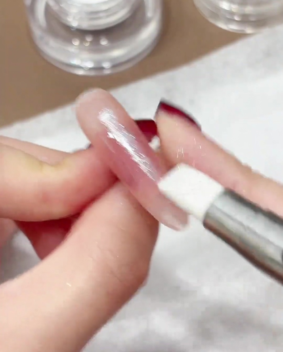Una penna in silicone che sfrega la polvere cromo iridescente sulla superficie di ununghia curata.