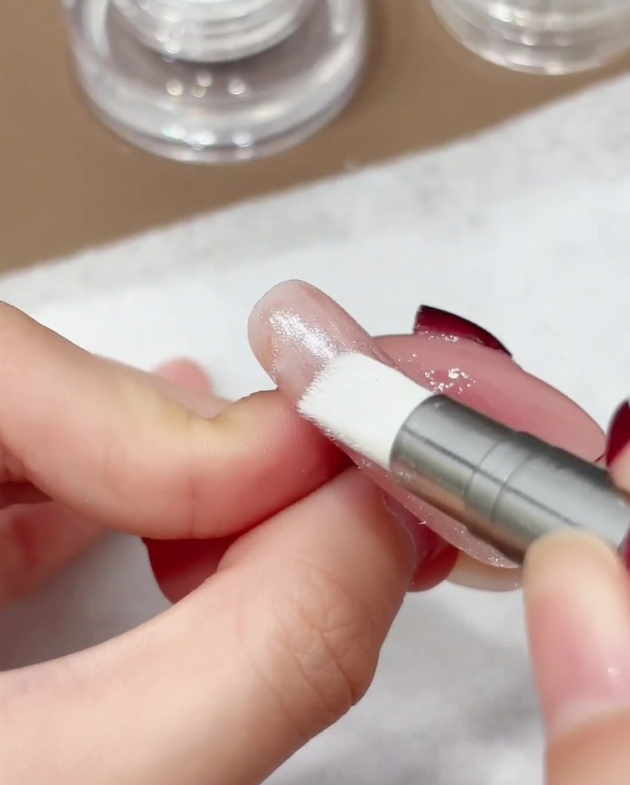 Primo piano di una penna applicatore con punta in silicone che lucida la polvere cromo aurora su una superficie ungueale.