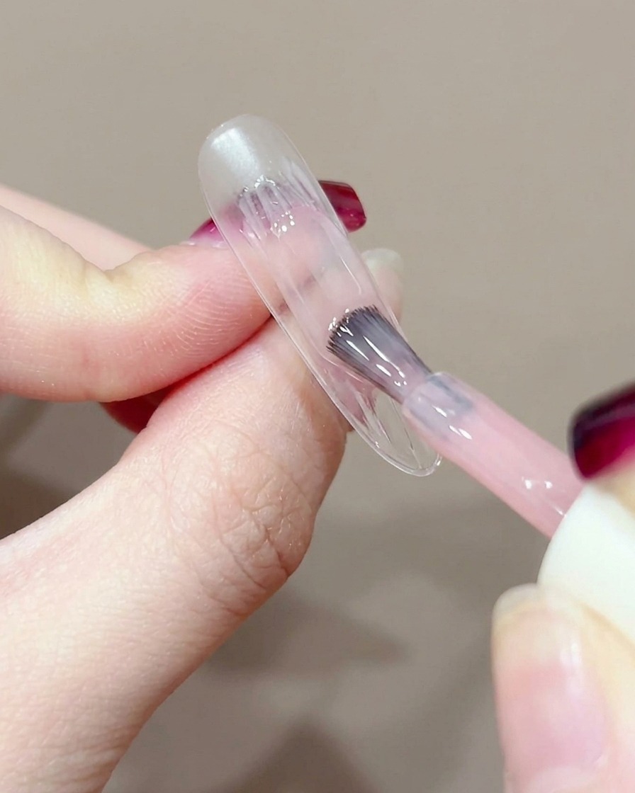 Primo piano di un pennello gel che applica una piccola goccia di gel pesca al centro dellunghia naturale.