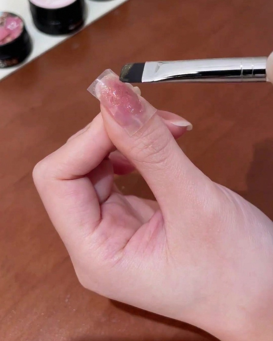 Un pennello che applica gel cat-eye oro sopra un adesivo a farfalla su ununghia.