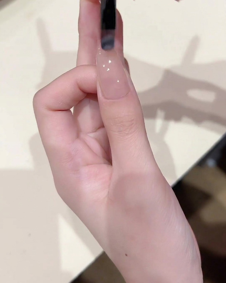 Primo piano di un pennello che applica uno strato sottile e uniforme di gel nude trasparente su ununghia già coperta da una base.
