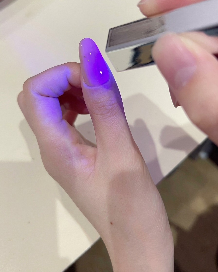 Una mano che utilizza una salvietta senza pelucchi per pulire la superficie di ununghia in gel polimerizzato.