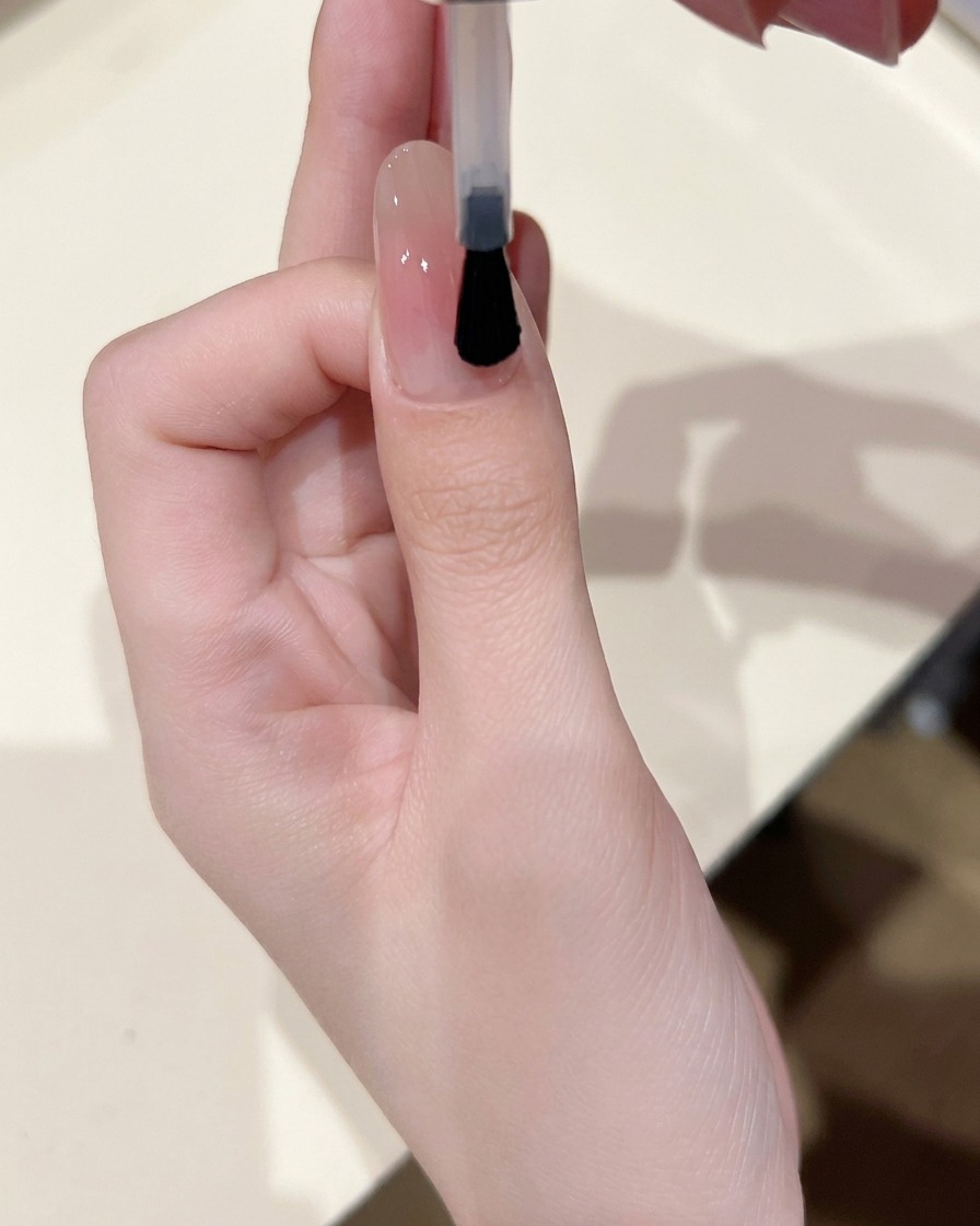 Un pennello per unghie che applica uno strato sottile di gel base lucido su ununghia con un centro blush delicato.