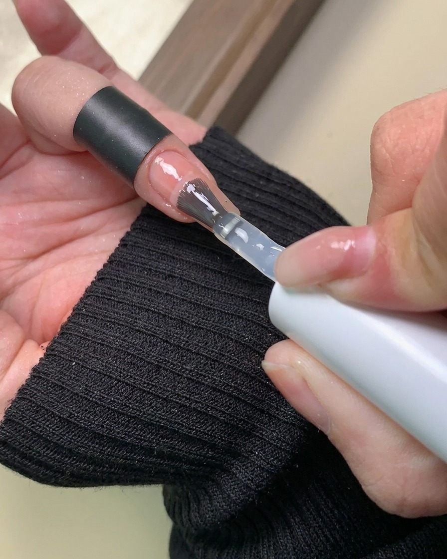 Un pennello che applica uno strato trasparente di base gel sopra il design a sfumatura di polvere aurora completato.