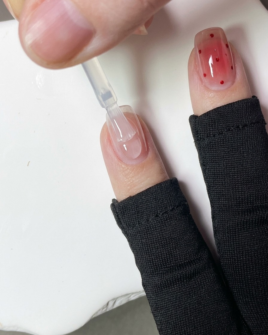 Un primo piano di un dotting tool che applica piccoli pois di gel rosso sulla superficie di ununghia.
