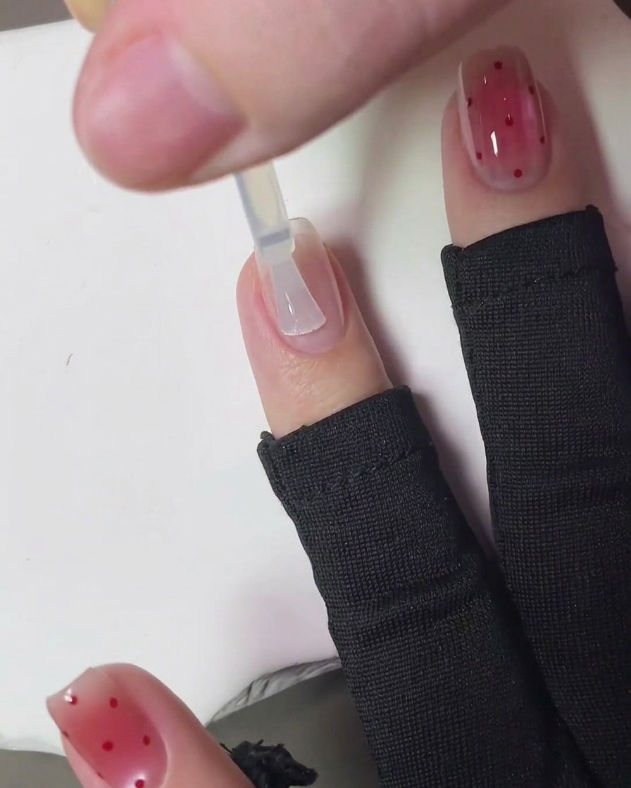 Un pennello che applica un top coat trasparente e lucido sopra la nail art finita a pois fragola.