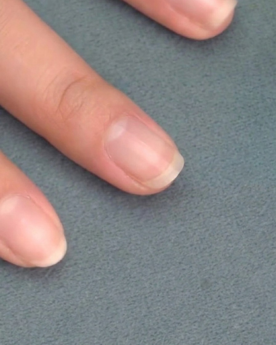 Un pennello applica uno strato sottile di smalto gel rosa tenue su ununghia naturale pulita.