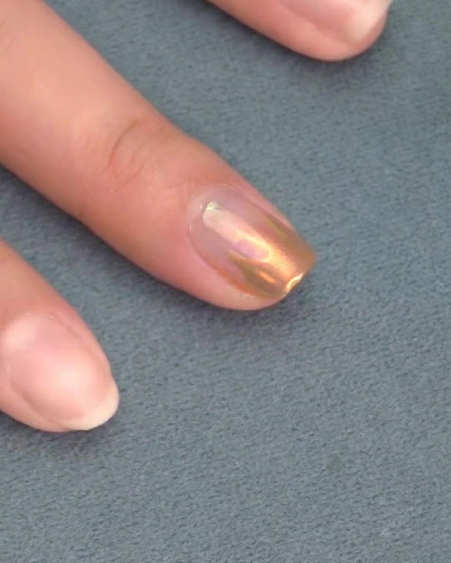 Un pennello applica un top coat trasparente finale sopra ununghia decorata con cromo.