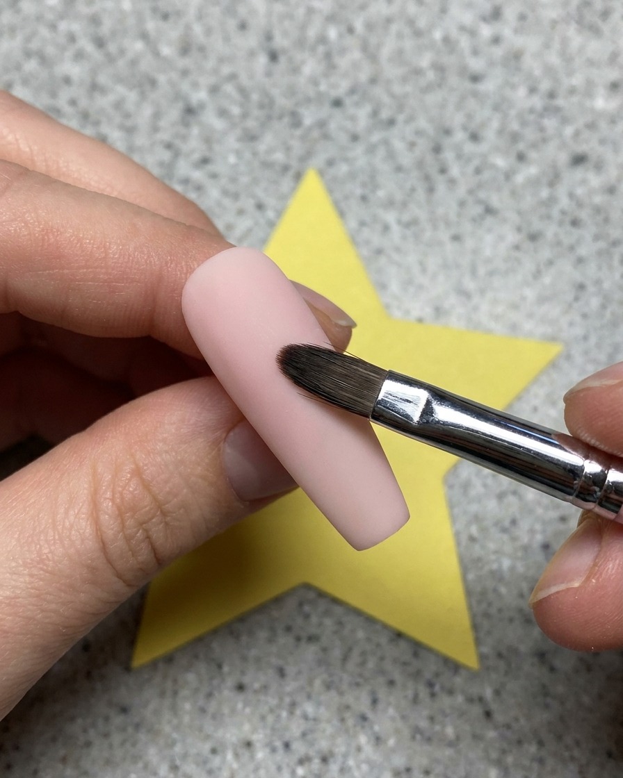 Primo piano di un gel trasparente applicato con un pennello su una base per unghie rosa.