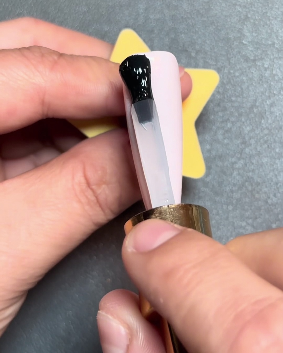 Un pennello applica una linea nera di smalto gel orizzontalmente sulla punta di ununghia rosa.