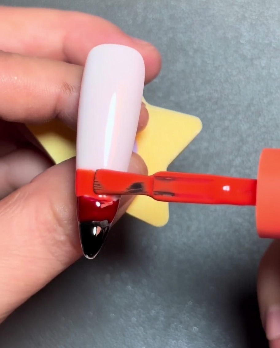 Un pennello applica una linea gialla di smalto gel sopra la striscia di gel arancione.