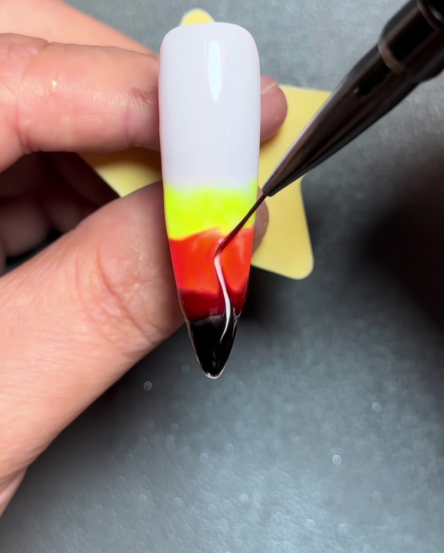 Un primo piano che mostra un pennello liner trascinare linee di colore verso lalto attraverso il gel bagnato, creando forme di fiamme.
