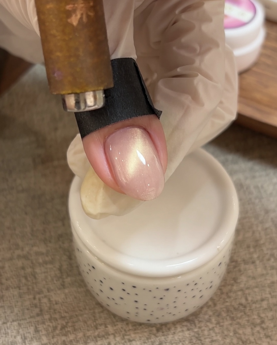 Una mano usa uno strumento magnetico per spingere le particelle scintillanti del gel cat eye verso la punta dellunghia.