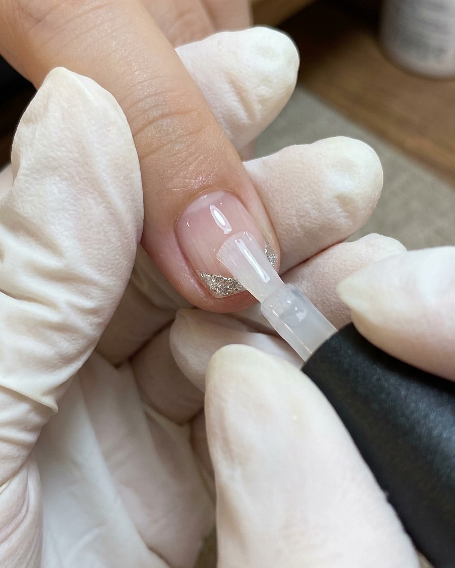 Un pennello applica uno strato di top coat trasparente su ununghia decorata con un cuore e sottili linee bianche e argento.