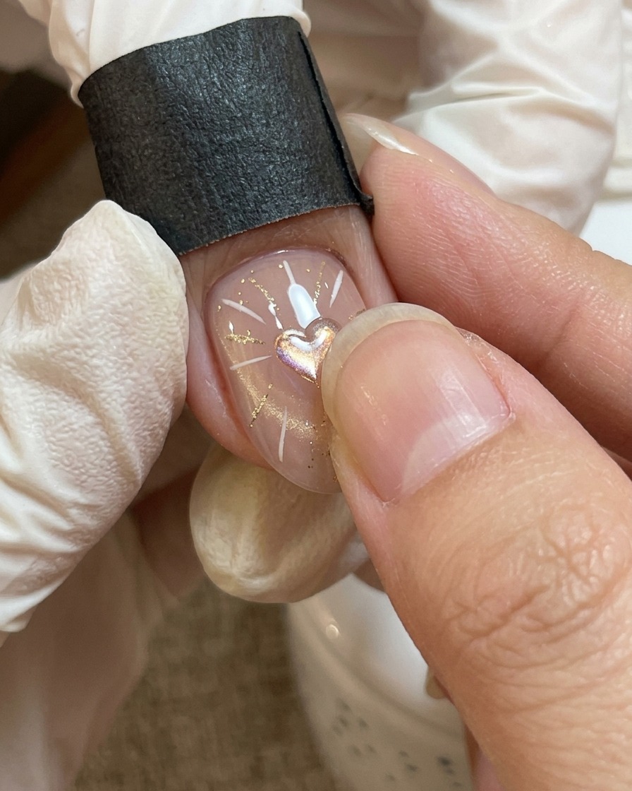 Vista ravvicinata di un processo di nail art in cui un gel trasparente più denso viene posizionato con cura sopra un motivo a cuore centrale.